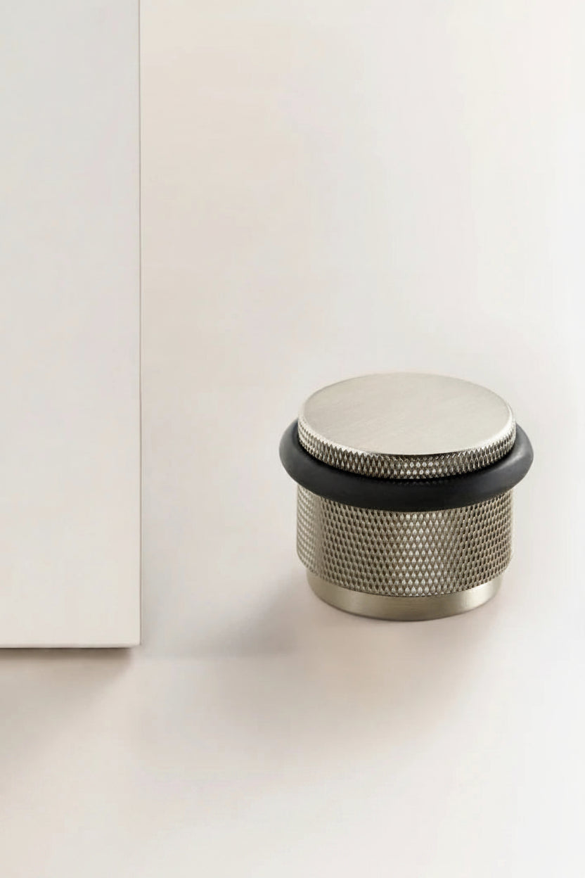 Adjustable knurled door stop with brushed metal body and black top ring, floor-mounted