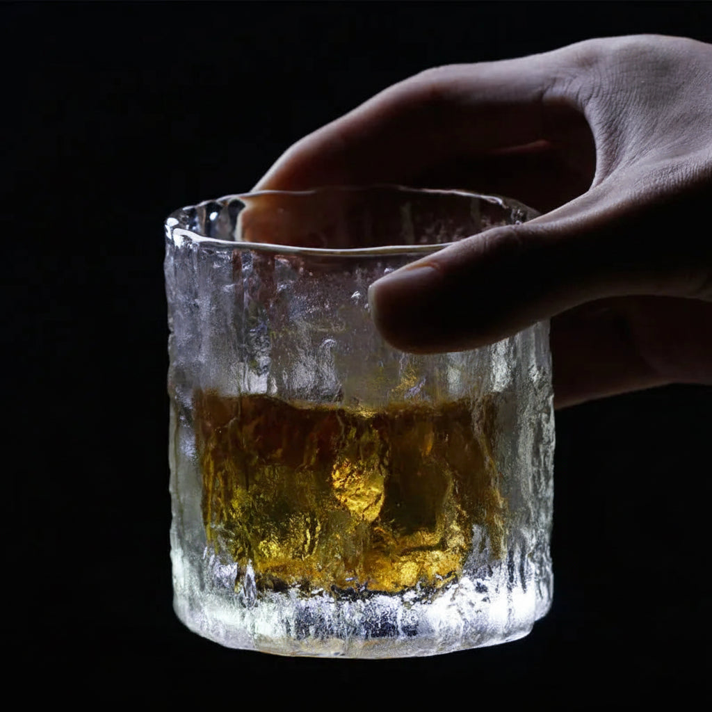 Hammered crystal rocks glass with amber drink, hand adjusting the rim.