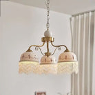 Gold three-head pendant light with white ceramic shades, brown floral trim, fringe tassels on chain