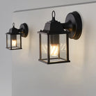 Set of black outdoor wall lantern lights with clear glass panels and warm bulbs