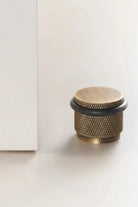 Adjustable knurled door stop with warm bronze body and black top ring, floor-mounted