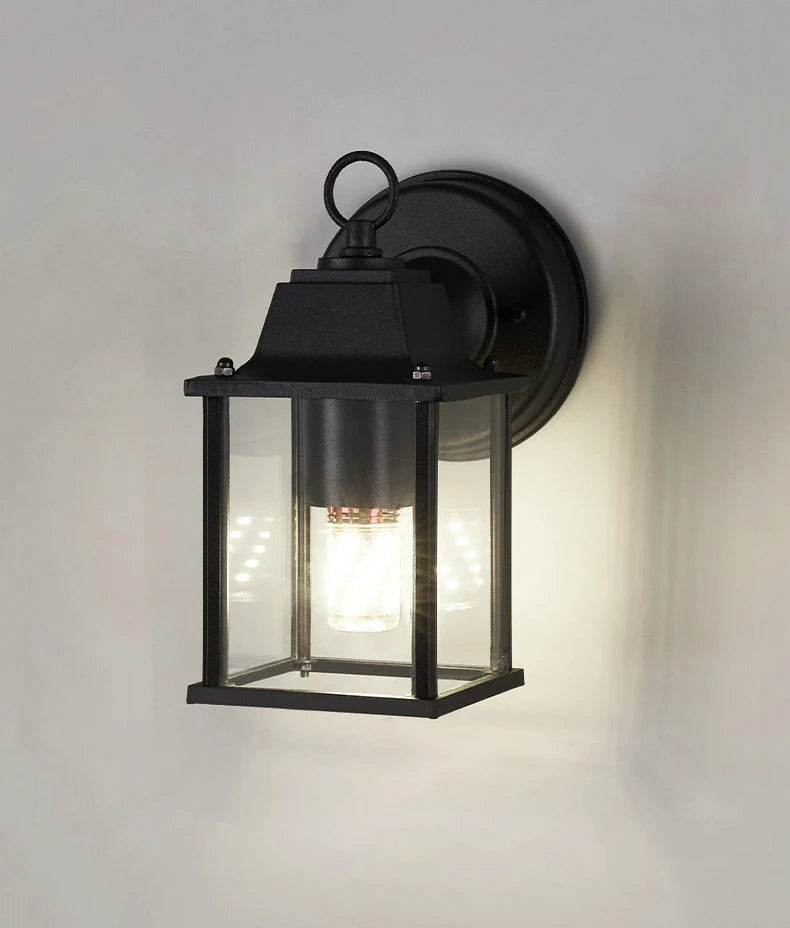 Black exterior wall sconce with clear glass lantern and warm light illumination