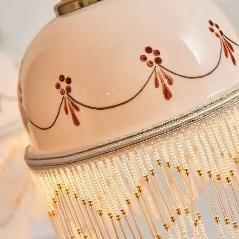 Close-up of white ceramic pendant shade with brown floral linework and golden fringe detailing