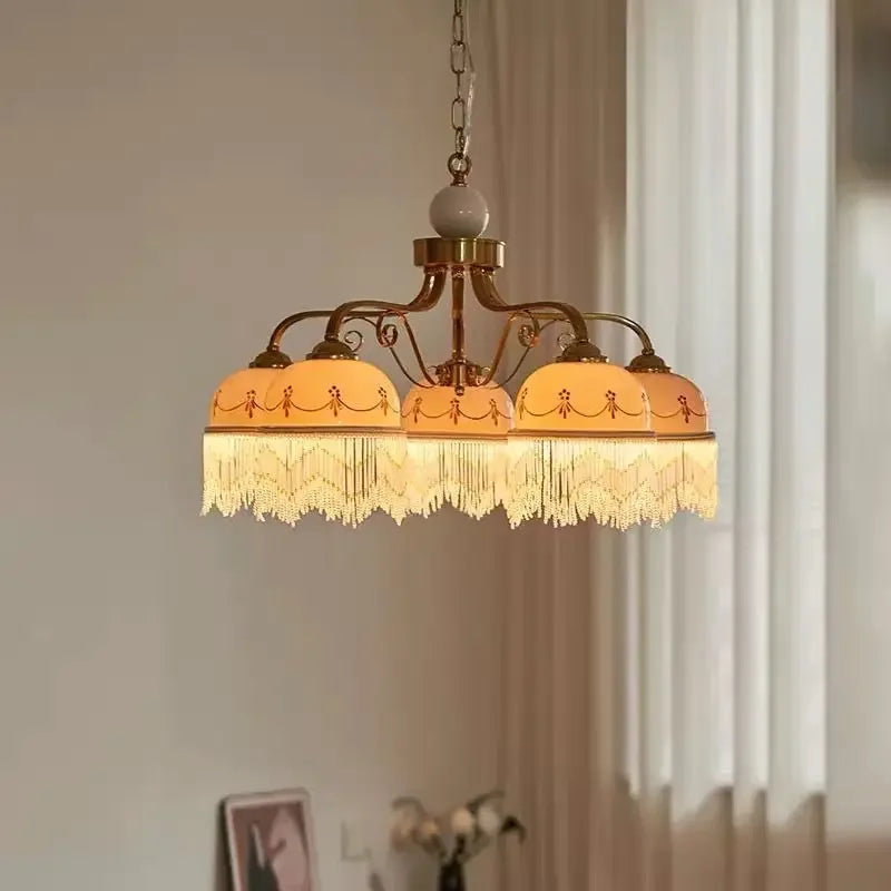 Gold three-head pendant light with white ceramic shades, brown floral trim, tassel fringe on chain