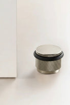 Adjustable knurled door stop with brushed metal body and black top ring, floor-mounted