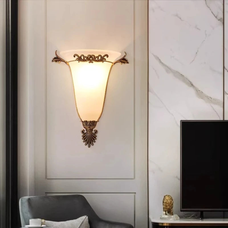 Decorative gold wall sconce with glowing frosted glass shade and carved metal crest