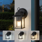 Black outdoor wall lantern light with clear glass sides and warm glowing bulb